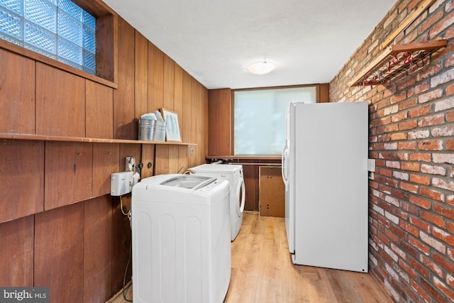 laundry area with brick wall, washer and dryer, light hardwood / wood-style floors, and wood walls