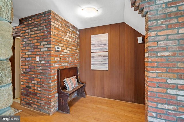 hallway featuring hardwood / wood-style flooring, lofted ceiling, brick wall, and wood walls