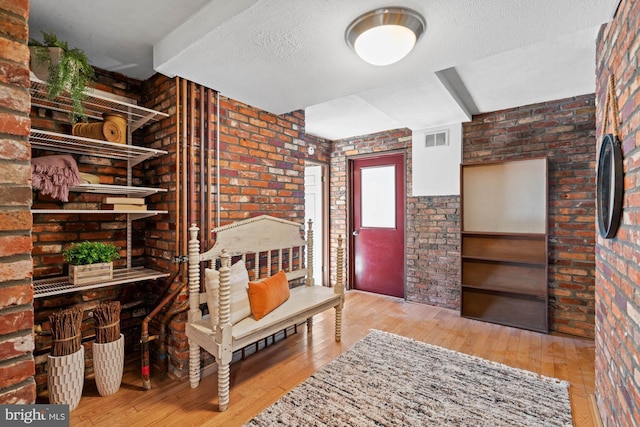 interior space featuring wood-type flooring, a textured ceiling, and brick wall