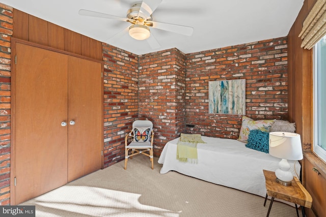 carpeted bedroom featuring ceiling fan, brick wall, and a closet