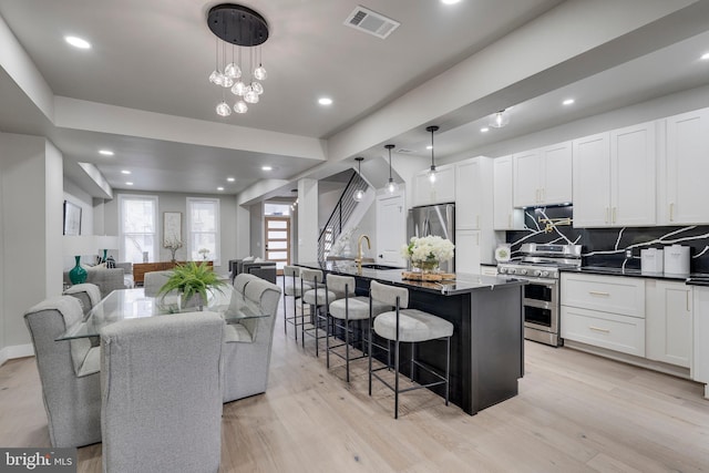 kitchen with hanging light fixtures, light hardwood / wood-style flooring, backsplash, a center island with sink, and appliances with stainless steel finishes