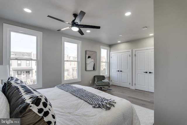 bedroom featuring light wood-type flooring, two closets, multiple windows, and ceiling fan