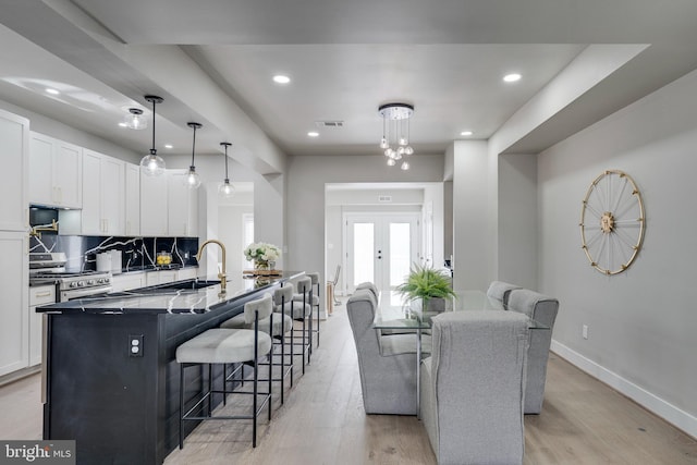 kitchen with a center island with sink, light hardwood / wood-style flooring, high end stainless steel range, white cabinetry, and hanging light fixtures