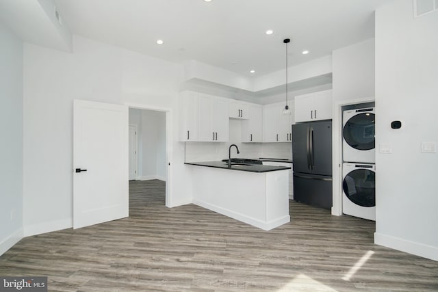 kitchen featuring light hardwood / wood-style floors, white cabinetry, black fridge, and stacked washing maching and dryer