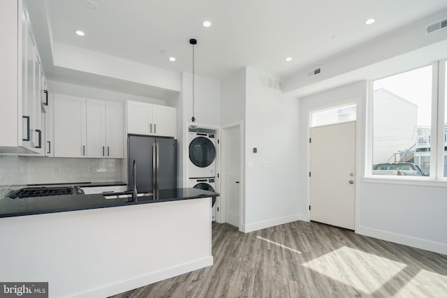 kitchen with sink, stacked washer and dryer, stainless steel fridge, decorative light fixtures, and white cabinetry