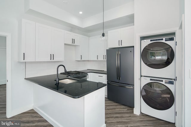 kitchen with stainless steel fridge, white cabinetry, hanging light fixtures, and stacked washer and clothes dryer