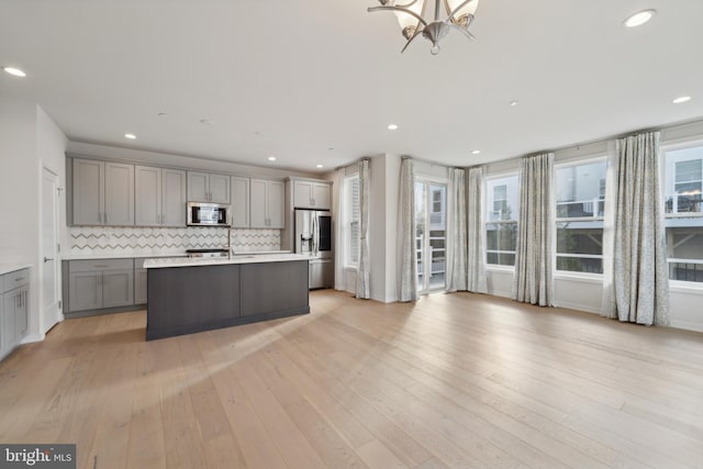 kitchen featuring gray cabinetry, decorative backsplash, light wood-type flooring, and stainless steel appliances