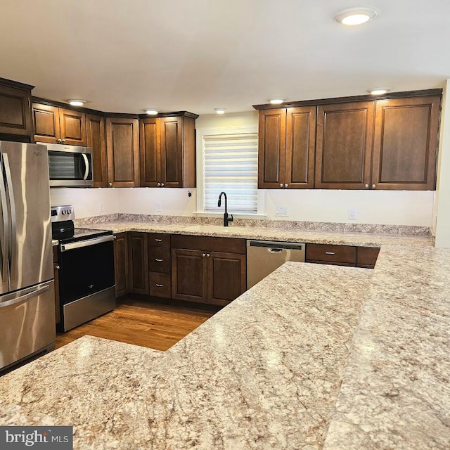 kitchen with sink, light stone countertops, stainless steel appliances, and light hardwood / wood-style flooring