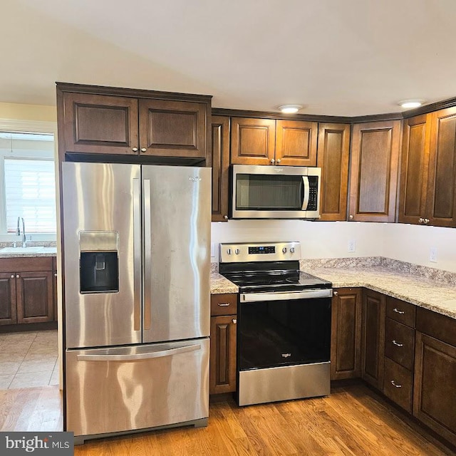 kitchen featuring light stone countertops, sink, stainless steel appliances, and light wood-type flooring