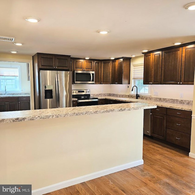 kitchen featuring sink, appliances with stainless steel finishes, light hardwood / wood-style floors, light stone counters, and dark brown cabinetry