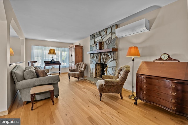 sitting room with a wall mounted air conditioner, a stone fireplace, and light hardwood / wood-style flooring