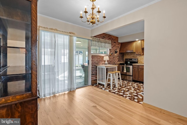 dining room with an inviting chandelier, ornamental molding, brick wall, and light hardwood / wood-style flooring