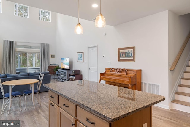 kitchen featuring pendant lighting, a center island, a towering ceiling, and light hardwood / wood-style flooring