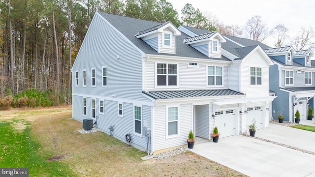 townhome / multi-family property with central air condition unit, driveway, a standing seam roof, an attached garage, and a front yard