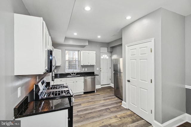 kitchen featuring sink, stainless steel appliances, dark hardwood / wood-style flooring, dark stone counters, and white cabinets