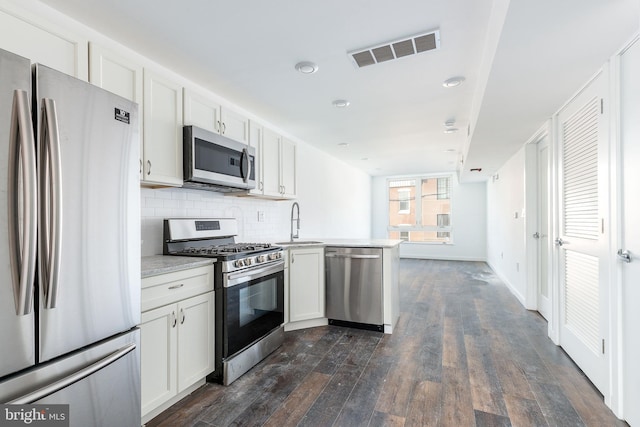 kitchen with kitchen peninsula, stainless steel appliances, sink, white cabinets, and dark hardwood / wood-style floors