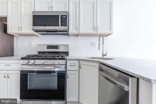 kitchen featuring sink, stainless steel appliances, tasteful backsplash, light stone counters, and white cabinets