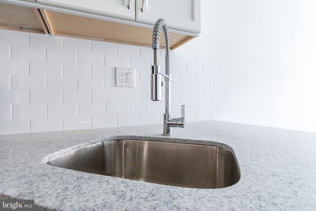 interior details with white cabinets, decorative backsplash, light stone countertops, and sink