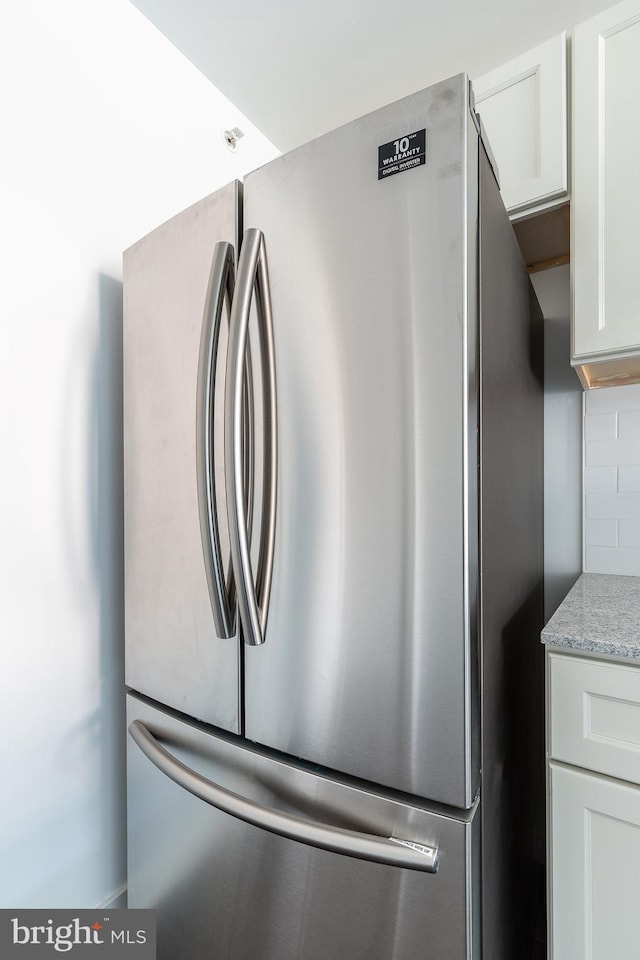 interior details with white cabinets, stainless steel fridge, backsplash, and light stone countertops