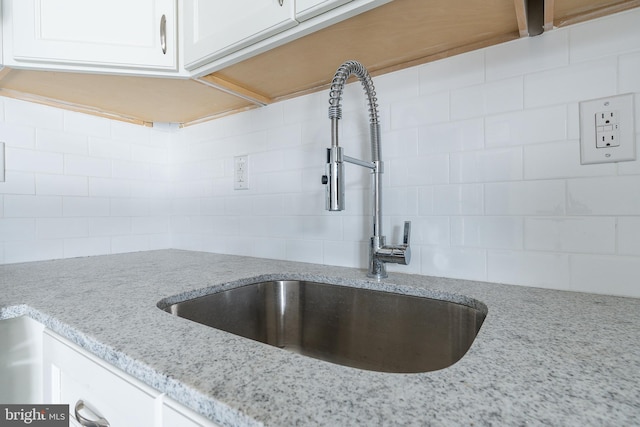 room details with white cabinets, backsplash, light stone countertops, and sink