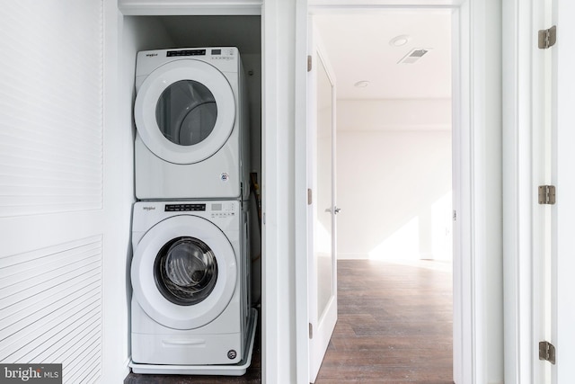 laundry area featuring stacked washer and dryer and dark wood-type flooring