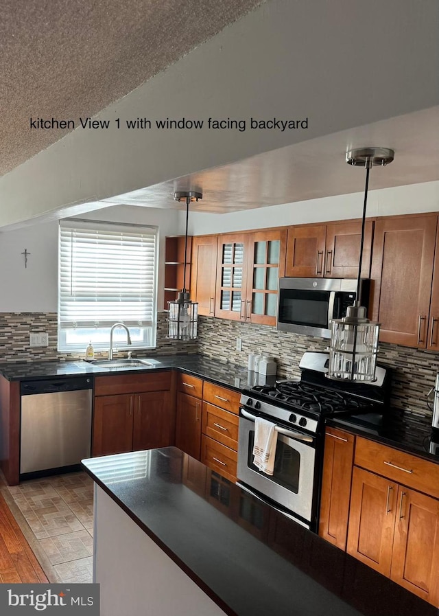 kitchen with decorative backsplash, appliances with stainless steel finishes, light wood-type flooring, sink, and hanging light fixtures