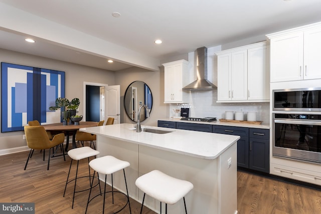 kitchen with white cabinets, a breakfast bar, wall chimney range hood, and dark wood-type flooring