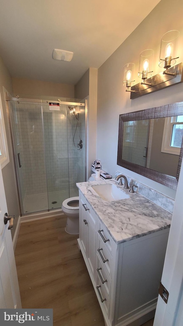 bathroom featuring hardwood / wood-style flooring, vanity, toilet, and a shower with shower door