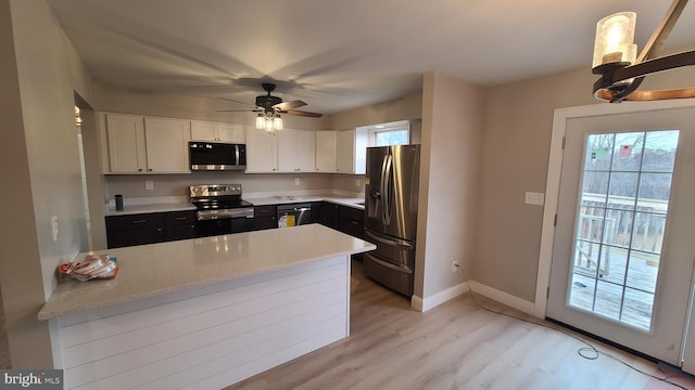 kitchen featuring pendant lighting, white cabinets, light wood-type flooring, light stone counters, and stainless steel appliances