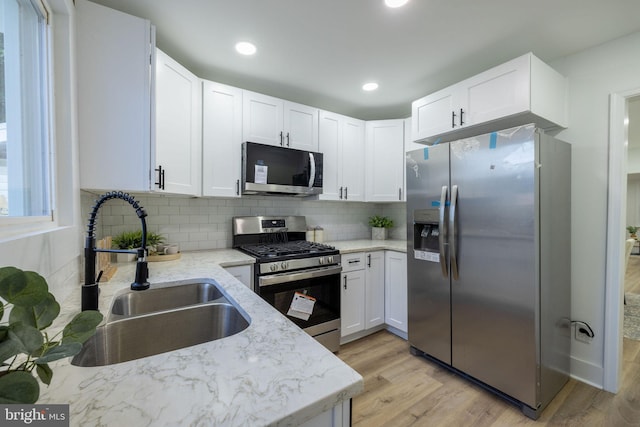 kitchen with sink, light hardwood / wood-style flooring, light stone countertops, white cabinetry, and stainless steel appliances