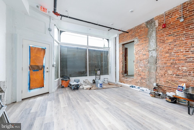 living room featuring a high ceiling, light wood-type flooring, and brick wall