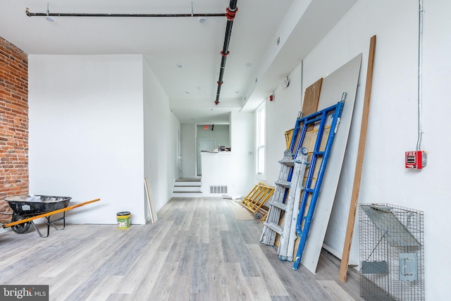 hallway featuring light hardwood / wood-style floors and brick wall