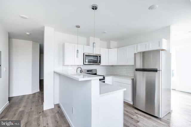 kitchen with white cabinets, hanging light fixtures, light hardwood / wood-style flooring, kitchen peninsula, and stainless steel appliances