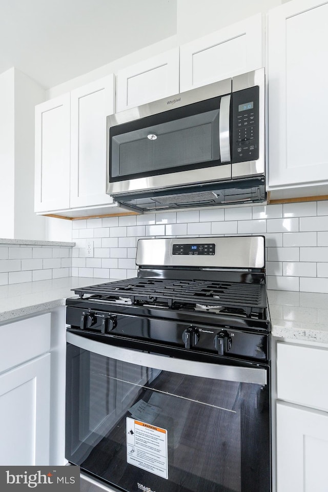 kitchen with white cabinets, appliances with stainless steel finishes, backsplash, and light stone countertops