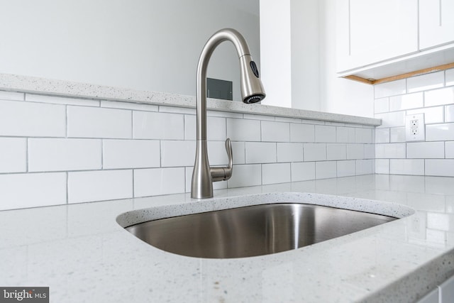 details featuring white cabinets, light stone counters, sink, and tasteful backsplash