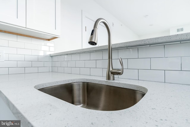 interior details featuring white cabinets, decorative backsplash, light stone counters, and sink