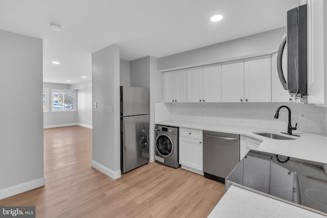 kitchen featuring sink, stainless steel appliances, light hardwood / wood-style floors, washer / dryer, and white cabinets