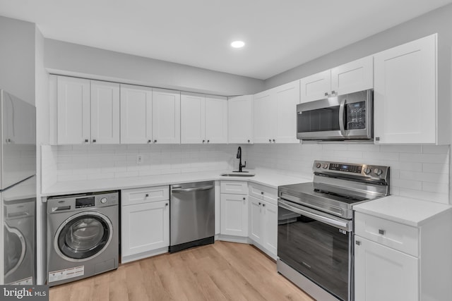 kitchen featuring appliances with stainless steel finishes, light wood-type flooring, washer / clothes dryer, and white cabinetry