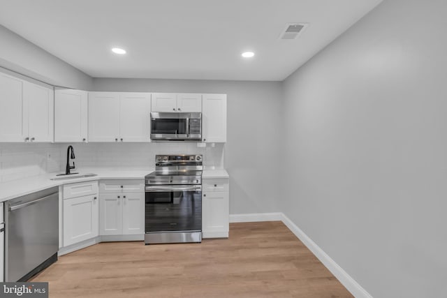 kitchen featuring light wood-type flooring, tasteful backsplash, stainless steel appliances, sink, and white cabinets