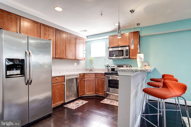 kitchen featuring stainless steel appliances, dark wood-type flooring, kitchen peninsula, pendant lighting, and a breakfast bar