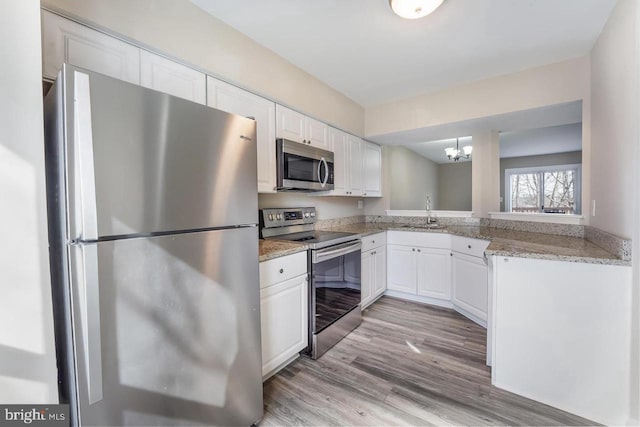 kitchen with hanging light fixtures, light hardwood / wood-style flooring, white cabinets, and stainless steel appliances