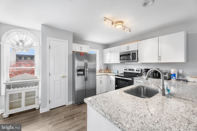 kitchen with sink, white cabinets, light wood-type flooring, and appliances with stainless steel finishes