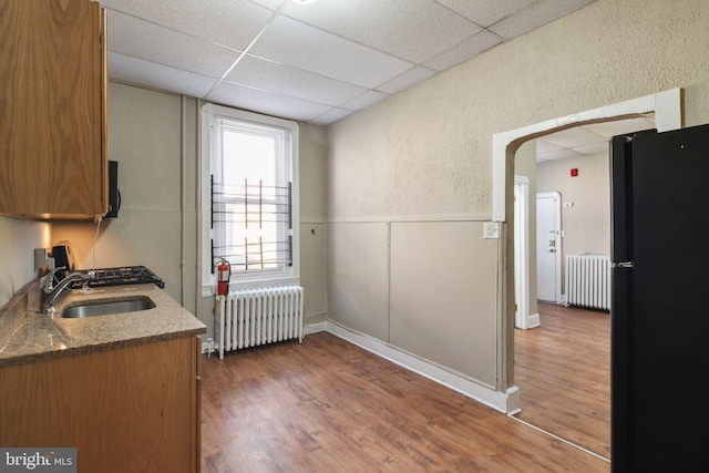 kitchen featuring radiator, black fridge, a drop ceiling, and sink