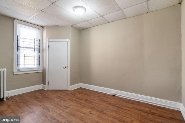 unfurnished room featuring hardwood / wood-style floors, a paneled ceiling, and radiator heating unit