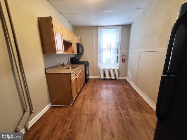 kitchen with sink, radiator, dark wood-type flooring, and black appliances