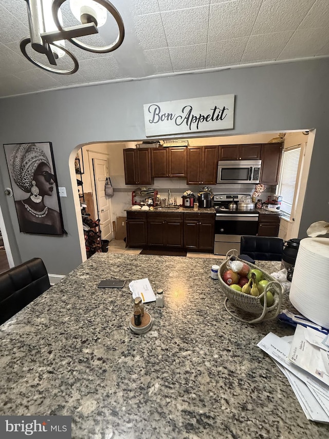 kitchen featuring dark brown cabinetry, sink, a notable chandelier, stone countertops, and appliances with stainless steel finishes