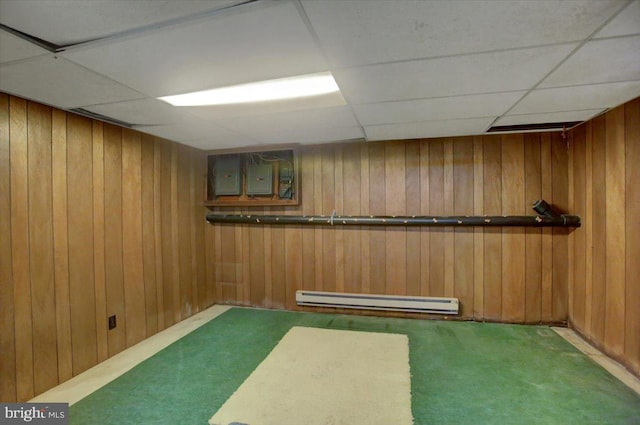 basement with carpet flooring, a baseboard radiator, a drop ceiling, and wood walls