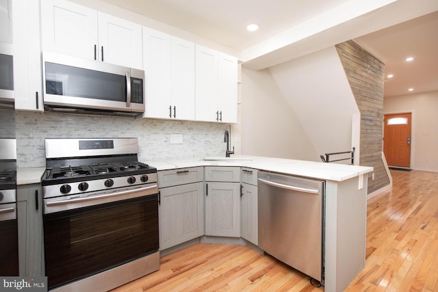 kitchen with kitchen peninsula, appliances with stainless steel finishes, sink, light hardwood / wood-style floors, and white cabinetry