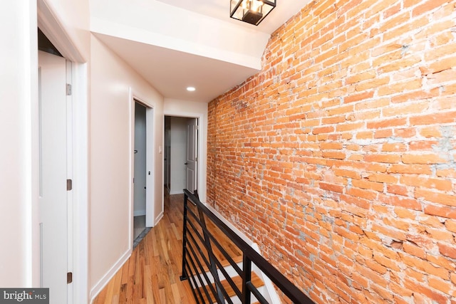 corridor with light hardwood / wood-style floors and brick wall