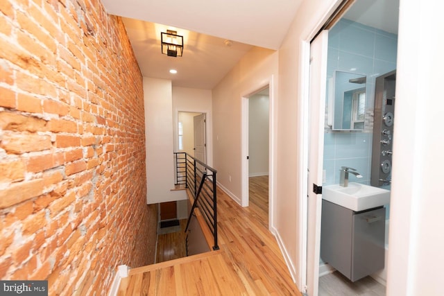 hallway featuring sink, brick wall, and light hardwood / wood-style flooring